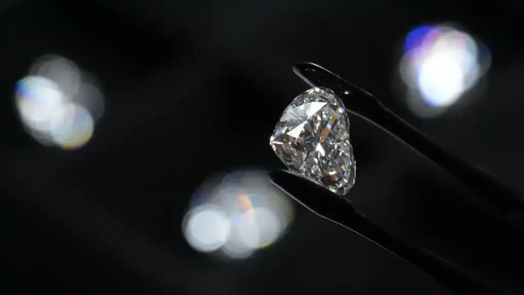 Rare Diamond Displayed Under Inspection | Brimco A large faceted diamond held by precision tweezers against a dark background reflecting light